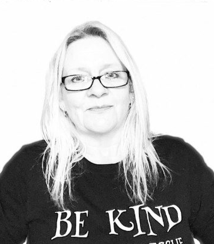 A black and white photo of Paws2Rescue team member Sarah-Jane wearing a jumper with the words "Be Kind" printed on the front